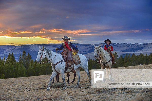 USA  Wyoming  two young cowboys riding in wilderness at sunset