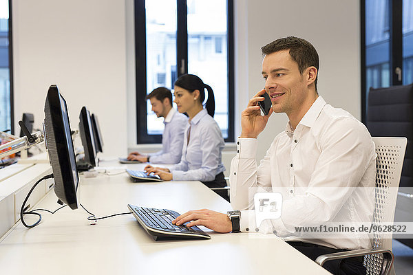 Man at desk on cell phone with colleagues in background