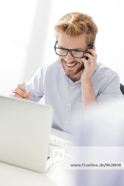 Smiling young businessman on cell phone at desk
