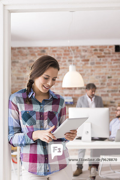 Lächelnde junge Frau mit digitalem Tablett im Büro