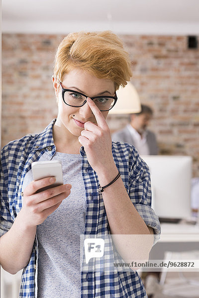 Lächelnde junge Frau mit Handy im Büro