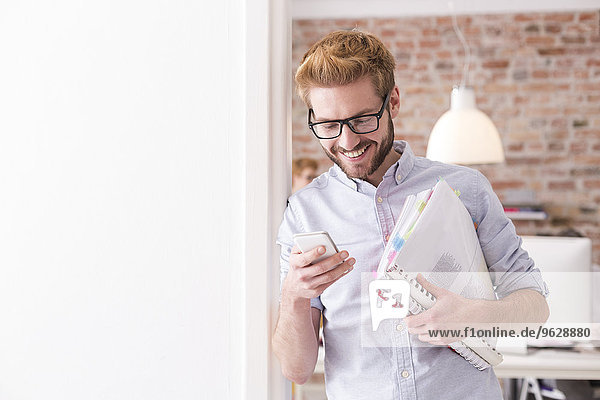 Smiling young man with cell phone and folders in office