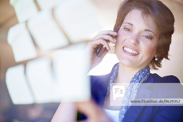 Portrait of female creative professional telephoning behind glass pane with adhesive notes