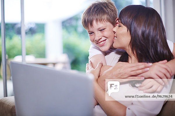 Mutter und Sohn zu Hause umarmen und benutzen Laptop