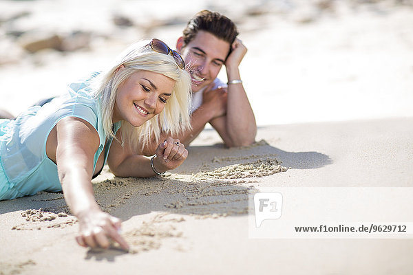 Young couple lying on the beach and drawing in the sand