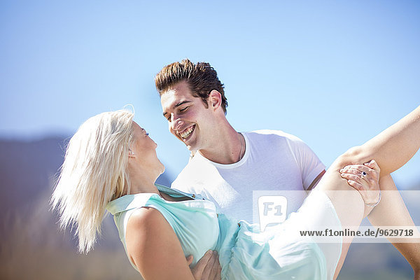 Young man carrying girlfriend under blue sky