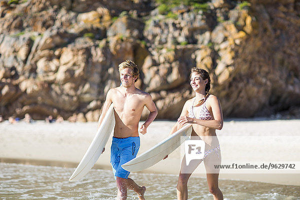 Junges Paar,  das mit seinen Surfbrettern ins Meer rennt