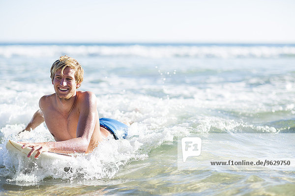 Glücklicher junger Mann auf dem Surfbrett im Meer liegend
