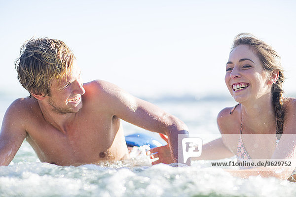 Glückliches junges Paar auf Surfbrettern im Meer liegend