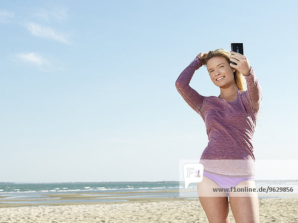 Junge Frau am Strand posiert für Smartphone Selfie  Altona  Melbourne  Victoria  Australien