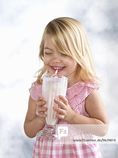 Portrait eines kichernden weiblichen Kleinkindes  das ein Glas Milch trinkt.