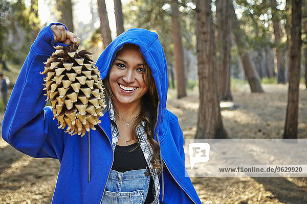 Porträt einer jungen Frau im Wald  die einen großen Kiefernzapfen hochhält  Los Angeles  Kalifornien  USA