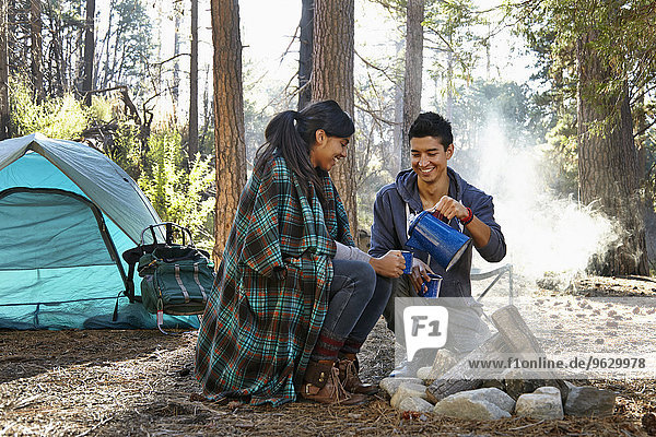Young couple pouring coffee by campfire in forest  Los Angeles  California  USA