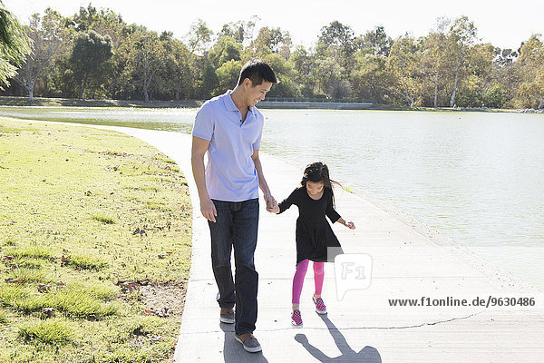 Erwachsener Mann und Tochter halten sich im Park an den Händen.