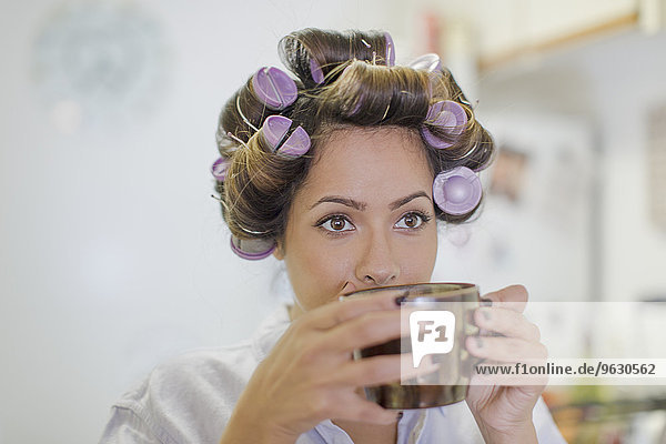Nahaufnahme einer erwachsenen Frau mit Haarrollen beim Kaffeetrinken