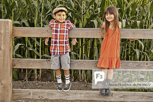 Porträt eines Jungen und eines Mädchens  die am Feldzaun stehen und sich festhalten.