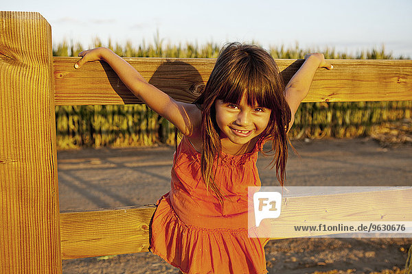 Porträt eines Mädchens  das sich an einem Holzzaun festhält.