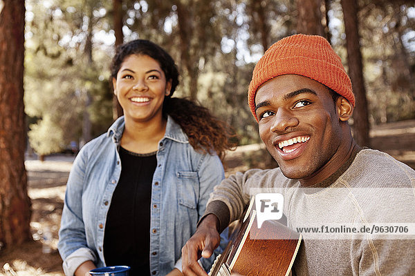 Junges Camping-Paar sitzt im Wald und spielt Akustikgitarre