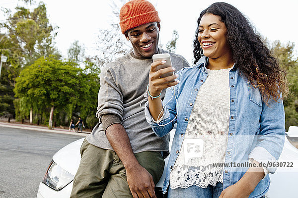 Young couple in car park reading smartphone texts