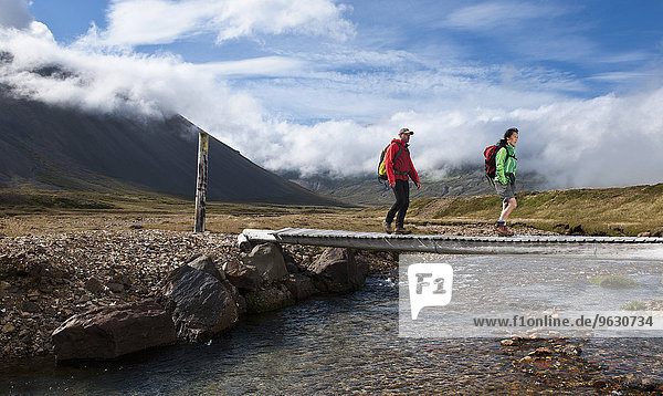 Mature hiking couple crossing wooden footbridge Breidvik Borgafjordur East East Iceland