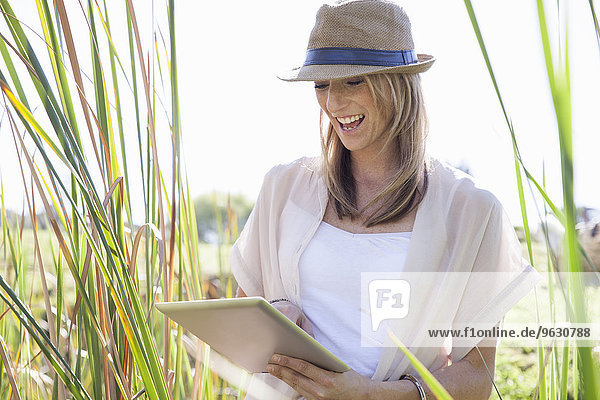 Mittlere erwachsene Frau im langen Gras sitzend,  mit digitalem Tablett