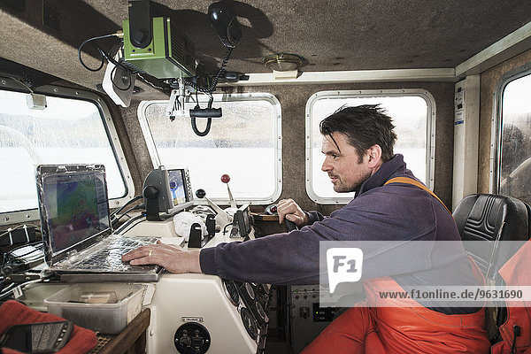 Fisherman driving fishing boat using laptop