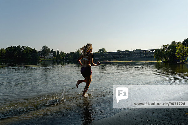 Teilweise gekleidete erwachsene Frau  die barfuß durch den See läuft