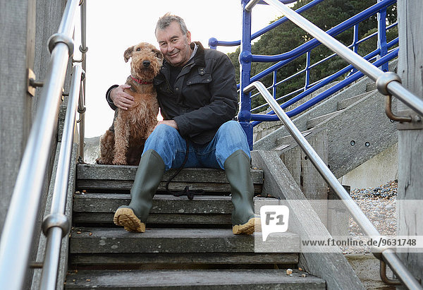 Porträt eines älteren Mannes mit Hund auf einer Treppe sitzend