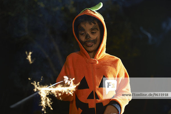 Junge im Halloween-Kürbiskostüm mit Wunderkerze im Garten bei Nacht