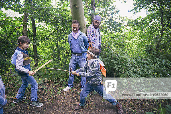Two men captured whilst boys have sword fight in forest