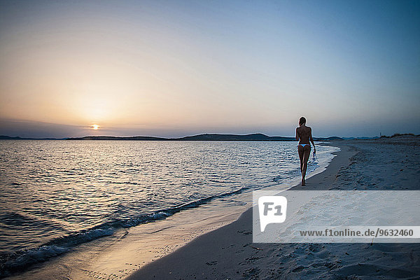 Rückansicht einer jungen Frau  die am Strand spazieren geht und Bikini-Top trägt  Cagliari  Sardinien  Italien