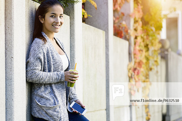 Portrait of young woman leaning against park wall drinking takeaway coffee