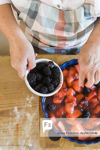 Woman pouring stewed fruit into a pie dish. Fresh blackberries.