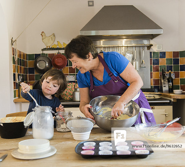 A woman and a child cooking at a kitchen table  making fairy cakes.