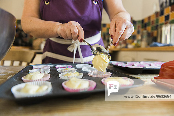 A woman at a kitchen table baking fairy cakes.