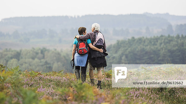A couple standing on a path looking at the view over wooded hills  with arms around each other.