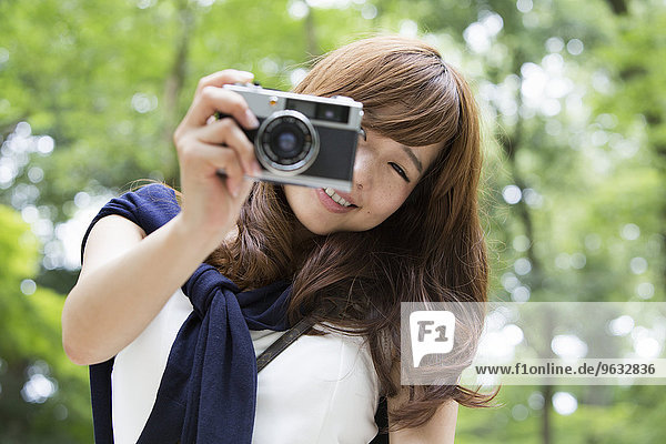 A woman in a Kyoto park holding a camera and laughing.