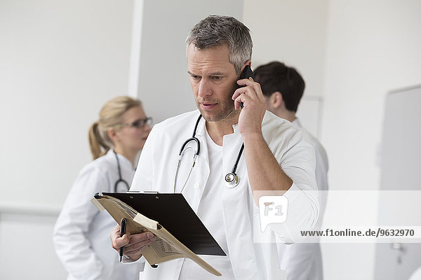 Doctor on phone with file while colleagues in background