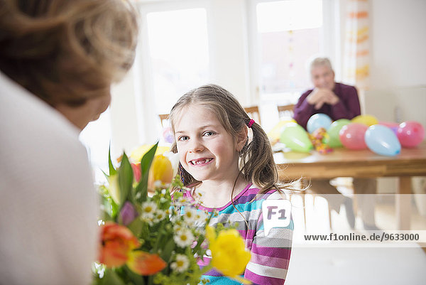 Granddaughter hand over bunch of flowers to her grandmother while grandfather in background