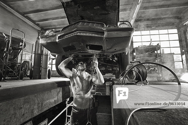 Muscular man mechanic using flex underneath car