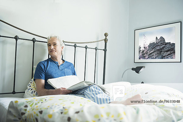 Mature man sitting with newspaper in bed  smiling