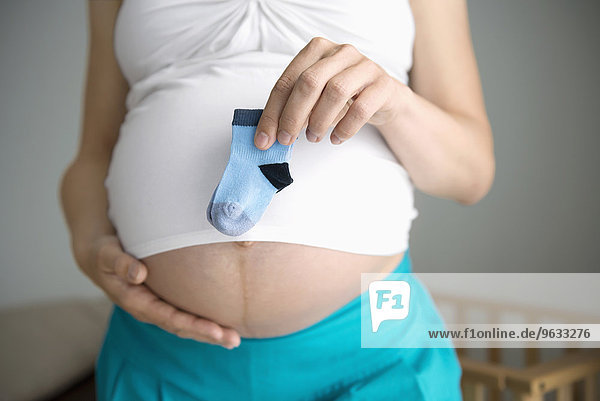 Woman pregnant holding baby socks stomach