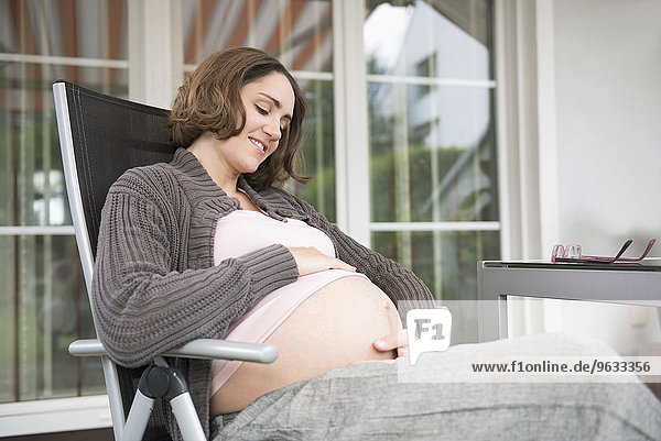 Woman pregnant sitting terrace holding stomach