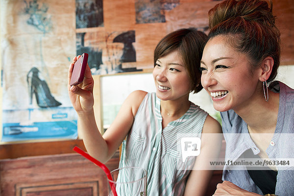 Two women looking at a cell phone  taking a selfie  sitting indoors.