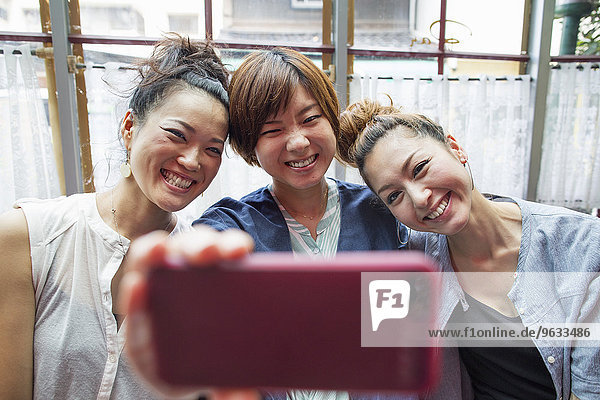 Three women looking at a cell phone  taking a selfie  sitting indoors.