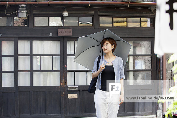 Frau  die im Freien steht und einen Regenschirm hält.