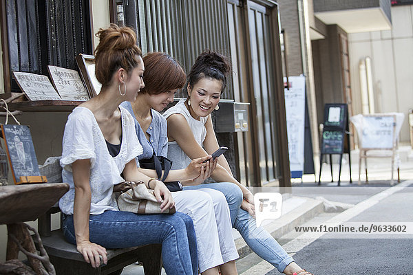Three women sitting outdoors  looking at cellphone.