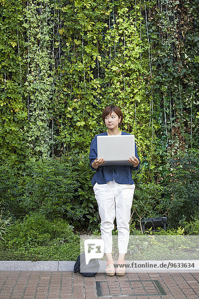 A woman holding a laptop in her arms and standing outdoors.