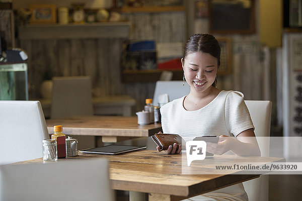 Woman sitting at a table in a cafe  holding the bill and her purse  smiling.