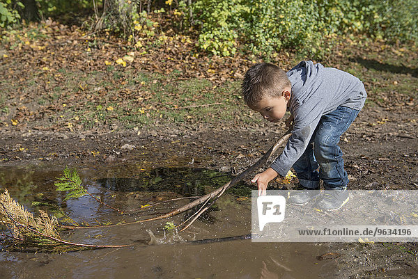Small boy holding branch splashing puddle fun